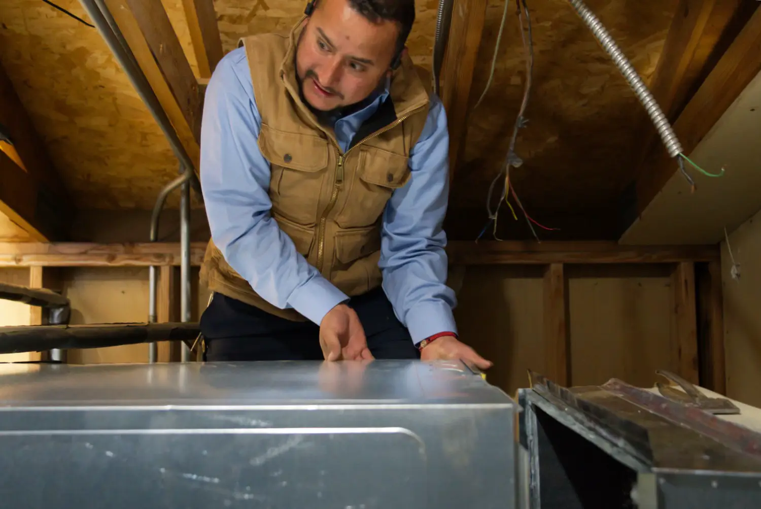 Nalk technician leaning over an HVAC unit in an attic