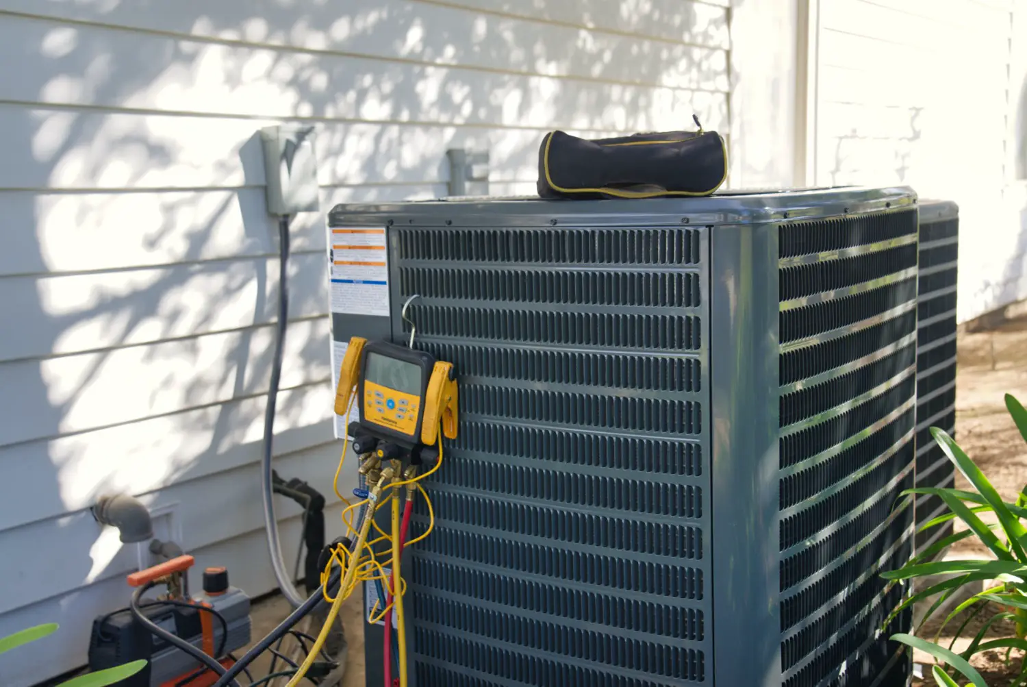 Outdoor air conditioning unit beside a house with a technician's gauge set connected