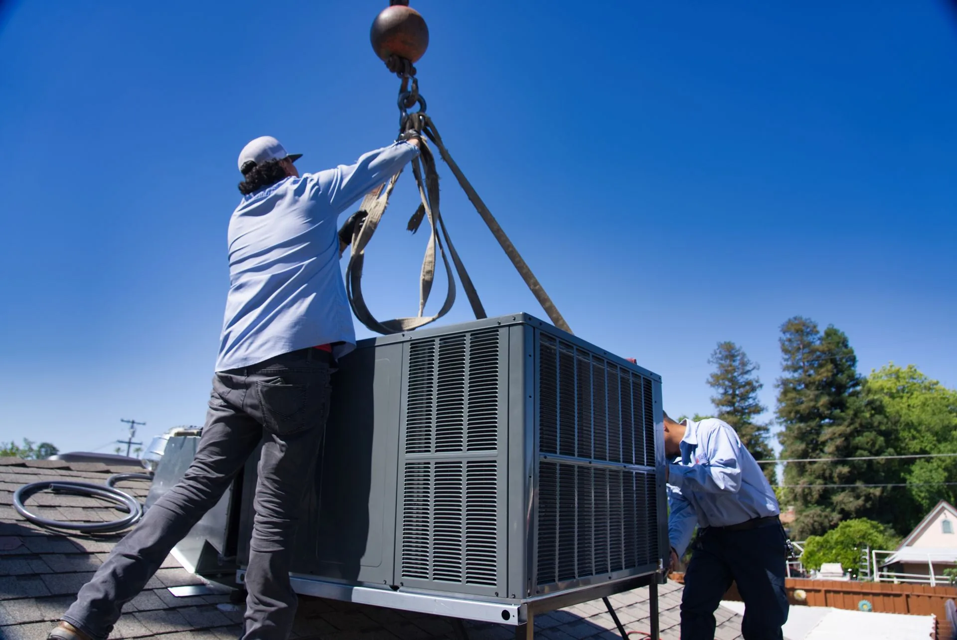 Two Nalk technicians guiding a rooftop air conditioner into place with a crane